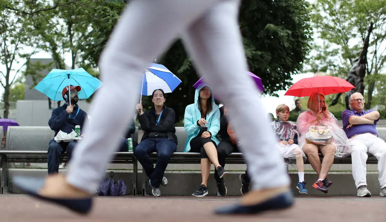 Sejumlah penonton mengunakan payung menunggu penundaan pertandingan akibat hujan selama putaran pertama turnamen tenis AS Terbuka 2017 di New York (29/8). (AP Photo / Michael Noble)