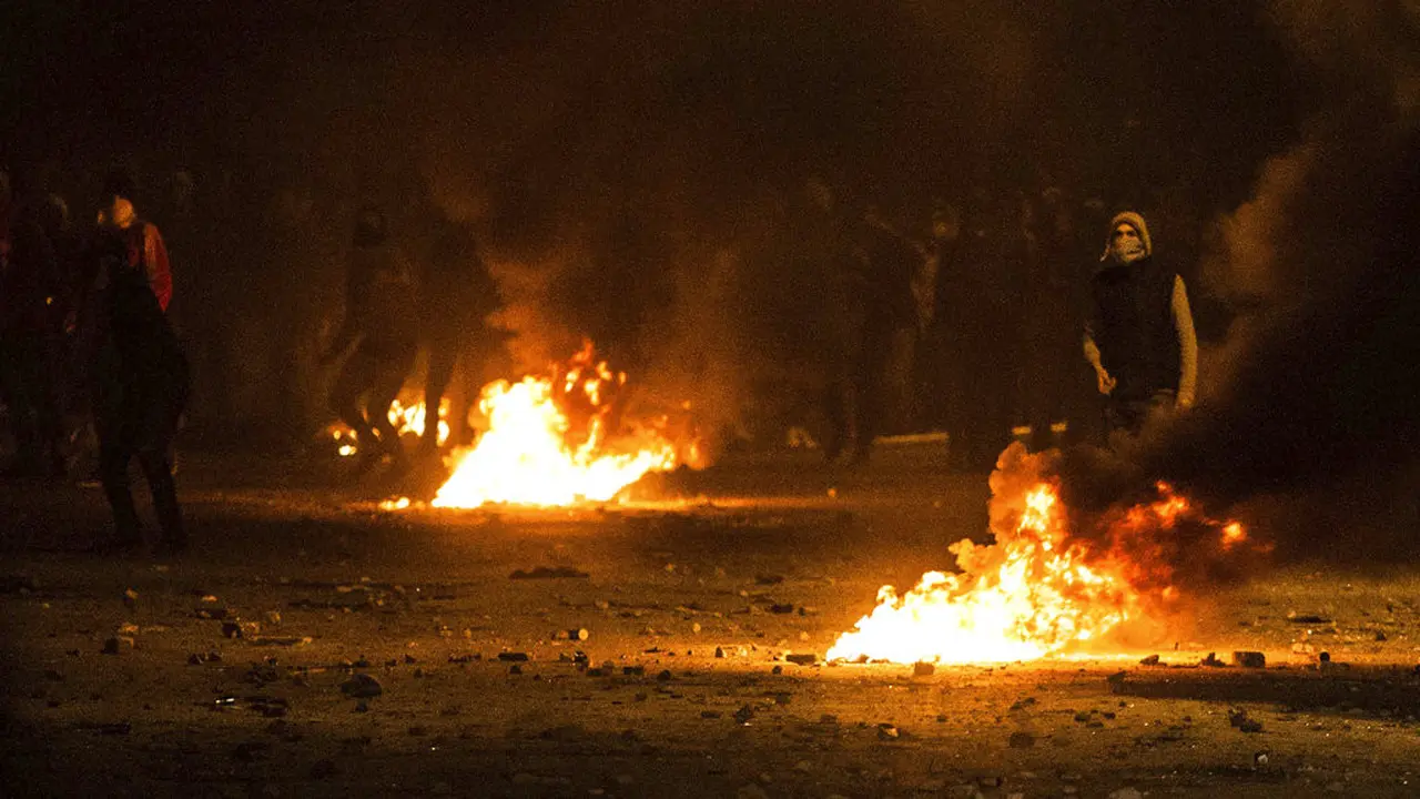Para pengunjuk rasa berada di balik barikade yang terbakar saat bentrok dengan polisi