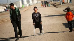 Jasim Abudllah berjalan menggunakan tongkat bersama temannya di kamp Debaga, di pinggiran Erbil, Irak (24/11). Walau hanya memiliki satu kaki, Jasim tetap semangat untuk bermain seperti teman-temannya. (Reuters/Mohammed Salem)