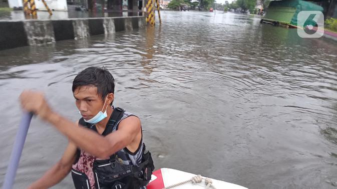 Seorang pria menggunakan perahu karet menerobos banjir di daerah Kaligawe, Kota Semarang, Selasa (9/2/2021). Banjir dengan ketinggian 30 hingga 90 cm ini melumpuhkan akses Semarang ke Demak dan sebaliknya. (Liputan6.com/Gholib)
