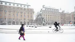 Pengendara sepeda melintasi Lapangan Gustav Adolfs saat salju turun di Stockholm (28/1/2021). Salju diperkirakan terutama menyebabkan masalah di jalan raya, dengan suhu berkisar di sekitar titik beku, yang berarti pengemudi dapat menghadapi es hitam secara tiba-tiba. (Henrik Montgomery/TT via AP)