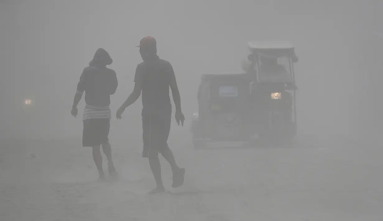 Penduduk berjalan saat gunung berapi Taal memuntahkan abu vulkanik di Lemery, provinsi Batangas, Filipina, Senin (13/11/2020). Erupsi gunung Taal memaksa puluhan ribu orang mengungsi serta membuat sekolah-sekolah dan toko di Manila tutup. (AP/Aaron Favila)