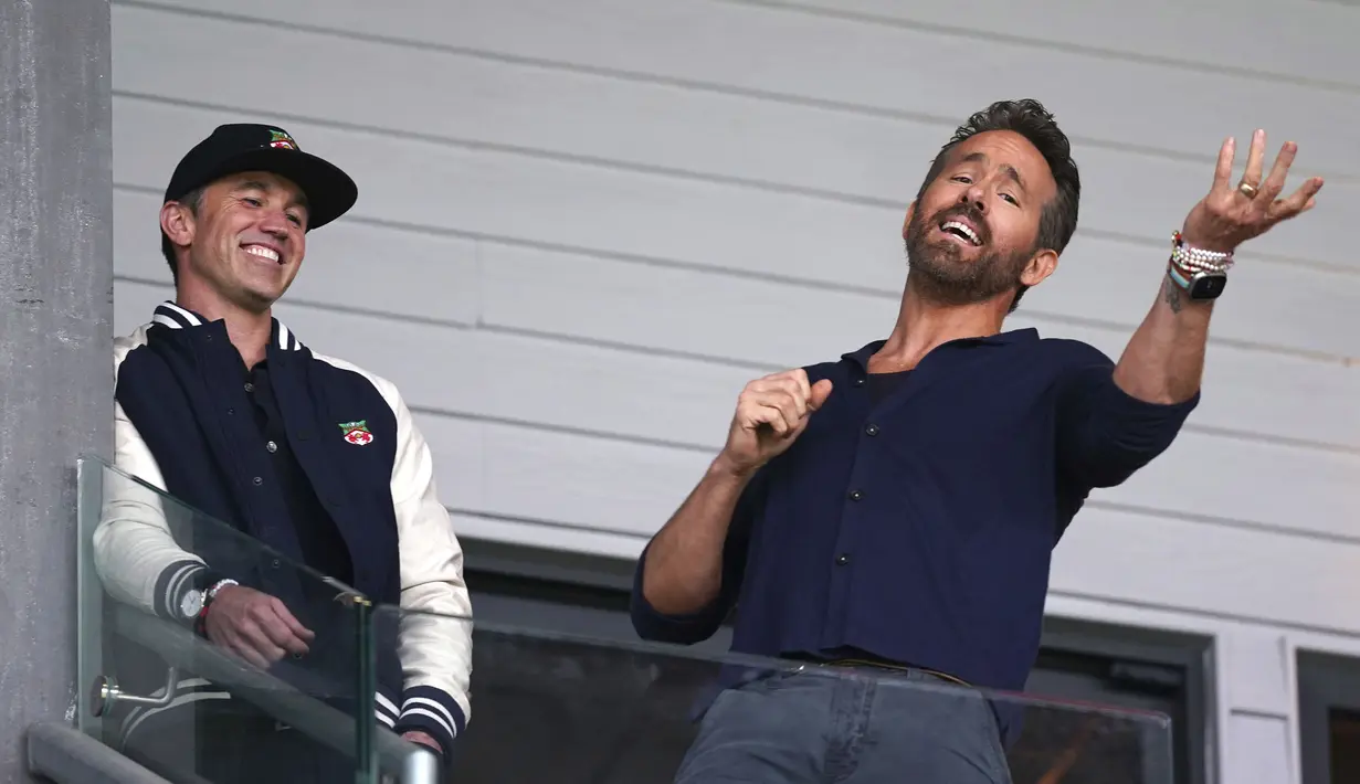 Aktor Hollywood, Ryan Reynolds (kanan) dan pemilik klub Wrexham, Rob McElhenney bercengkrama saat laga English National League antara Wrexham melawan Boreham Wood di Racecourse Ground Stadium, Wrexham, Wales, Sabtu (22/04/2023). Wrexham menang dengan skor 3-1 dan berhasil promosi ke Liga Dua Inggris. (AP/PA/Martin Rickett)