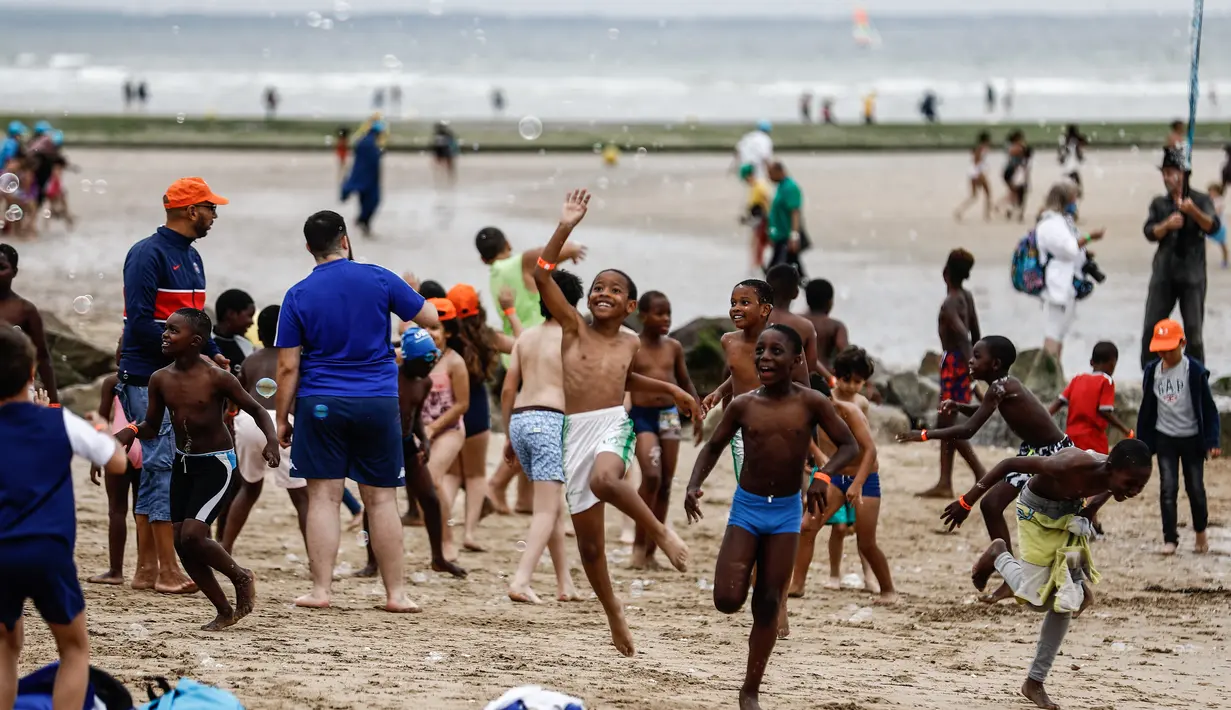 Anak-anak bermain dengan gelembung di pantai Cabourg, barat laut Prancis (18/8/2021). Seratus bus meninggalkan wilayah Paris dari delapan departemen Ile-de-France dengan 5.000 anak muda dari Ile-de-France dalam situasi genting yang belum sempat berangkat musim panas ini. (AFP/Sameer Al-Doumy)