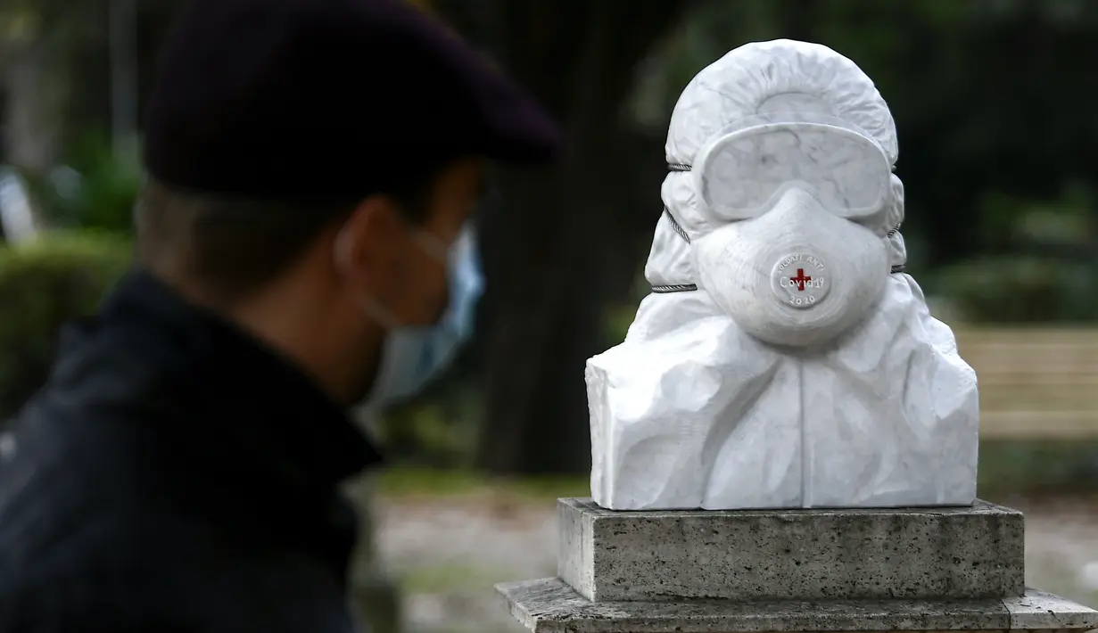 Seorang pria yang memakai masker wajah berjalan di dekat patung marmer yang didedikasikan untuk dokter, perawat, dan petugas kesehatan tanpa judul "Tentara anti Covid-19", di Taman Pincio di Roma tengah (4/11/2020). (AFP/Filippo Monteforte)