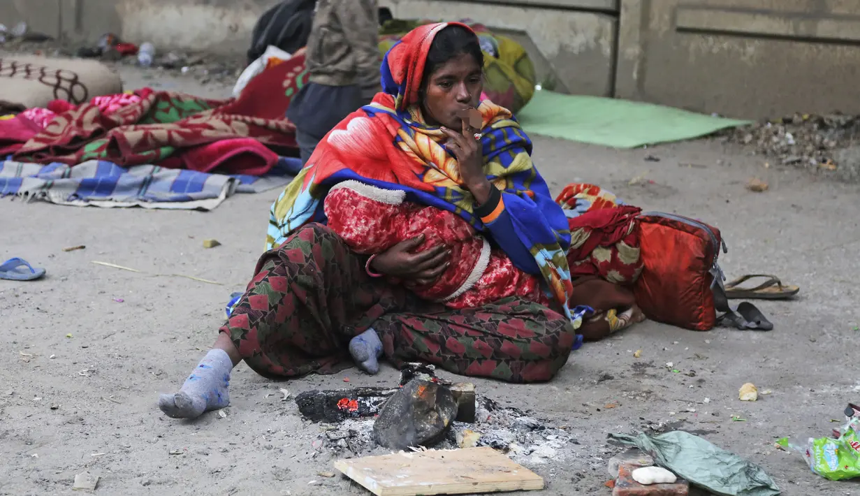 Seorang wanita tunawisma merokok sambil duduk dekat api unggun untuk menghangatkan diri di bawah jembatan layang di Jammu, India, Sabtu (28/12/2019). Sekitar 800 juta orang di India hidup dalam kemiskinan. (AP Photo/Channi Anand)
