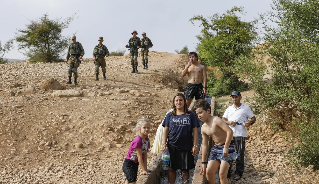Tentara Israel berjaga-jaga saat warganya asyik bermain air di sebuah kanal kecil di Desa Al-Auja selama perayaan keagamaan Yahudi dalam Festival Sukkot di Tepi Barat (17/10/2019). (AFP Photo/Menahem Kahana)