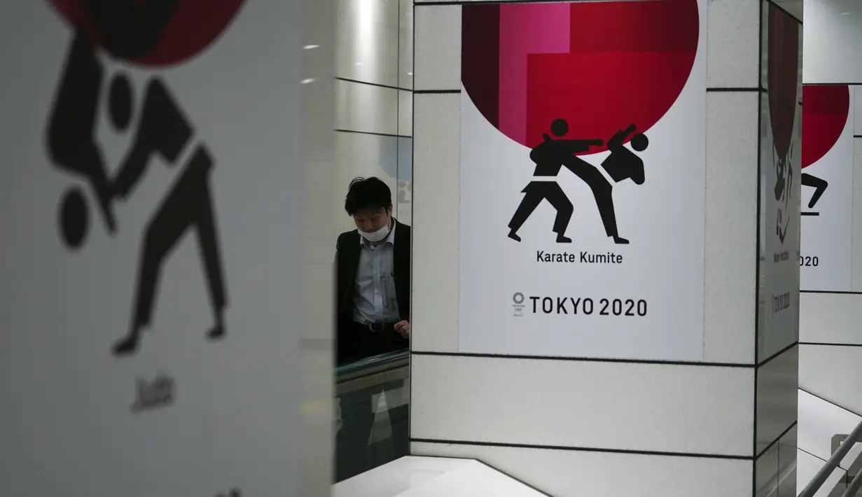 Seorang pria yang mengenakan masker pelindung untuk mencegah penyebaran virus corona berjalan di depan iklan Olimpiade Tokyo 2020 di Tokyo, Rabu (17/3/2021). Ibukota Jepang mengonfirmasi lebih dari 400 kasus virus korona baru pada hari Rabu. (AP Photo/Eugene Hoshiko)