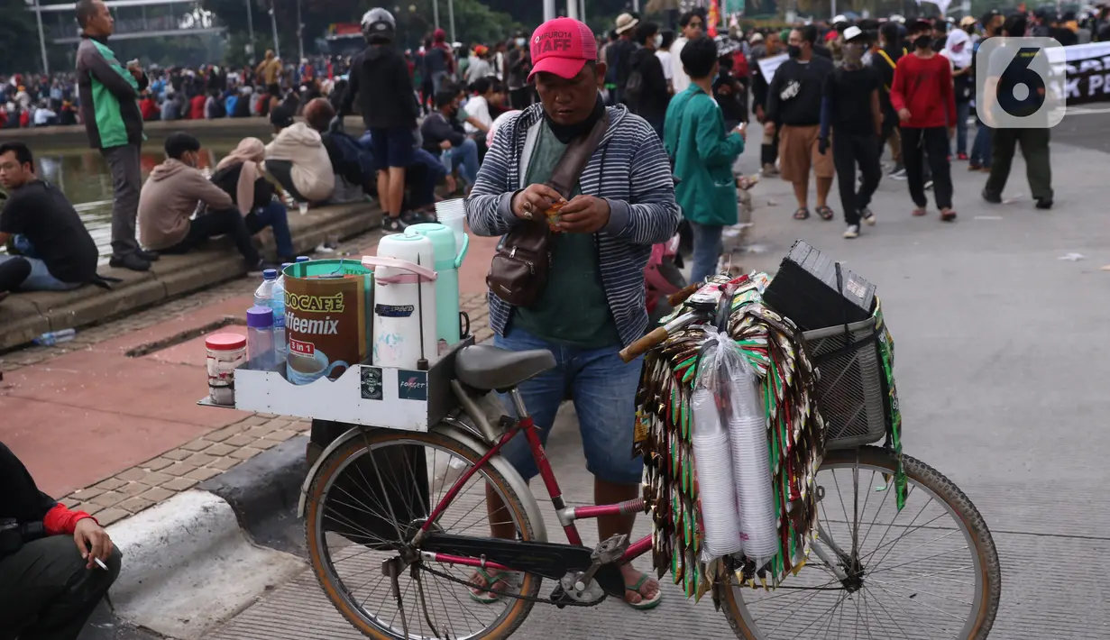 Pedangang membuat minuman untuk massa aksi saat demo penolakan omnibus law di kawasan Patung Kuda, Jakarta, Selasa (20/10/2020). Para pedagang kaki lima memanfaatkan moment aksi massa untuk mencari ke untungan meskipun sangat membahayakan bagi keselamatan mereka. (Liputan6.com/Angga Yuniar)