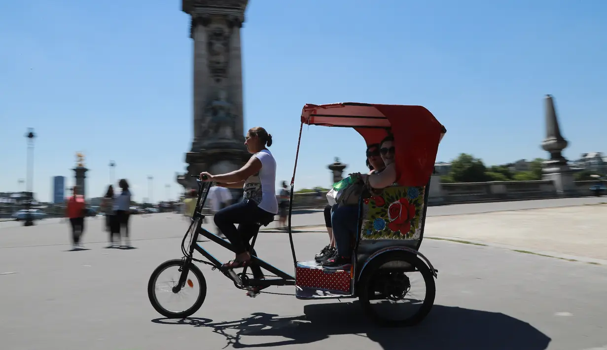 Wisatawan tersenyum saat menaiki becak berkeliling kota Paris, Prancis, (7/7). Wisatawan dibuat betah berlama-lama dengan desain becak di Paris ini. (AFP Photo/Jacques Demarthon)