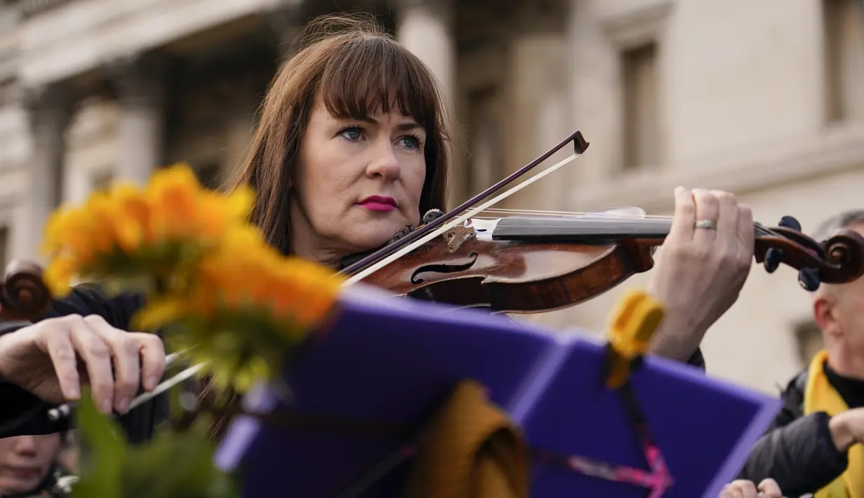 Anggota orkestra bermain sebagai bagian dari demonstrasi anti-perang menyusul serangan Rusia terhadap Ukraina di Trafalgar Square, London, Minggu (6/3/2022).  Flashmob yang terdiri dari 200 musisi klasik itu untuk menunjukkan dukungan terhadap Ukraina setelah invasi Rusia. (AP Photo/Alberto Pezzali)