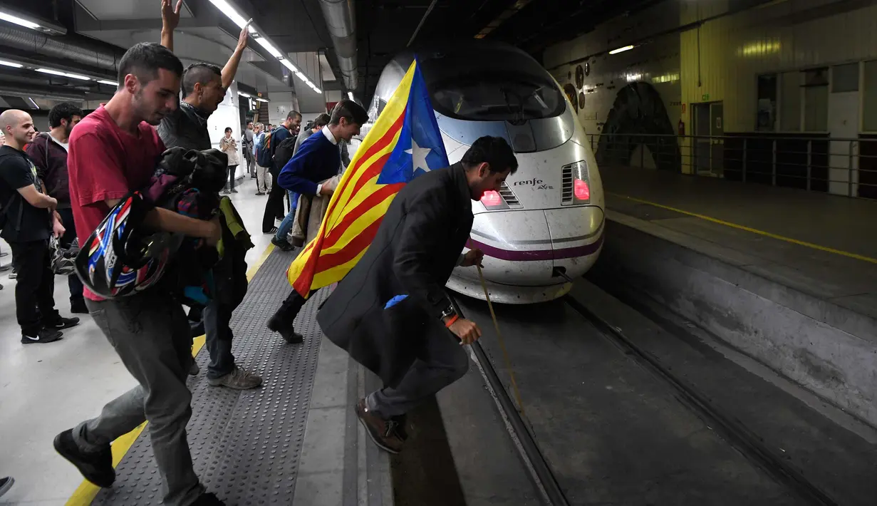 Pengunjuk rasa membawa bendera Catalonia melompat ke jalur kereta api di Stasiun Sants di Barcelona (8/11). Pengunjuk rasa memblokir jalan dan jalur kereta api setelah para pemimpin separatis ditahan di Madrid. (AFP Photo/Lluis Gene)