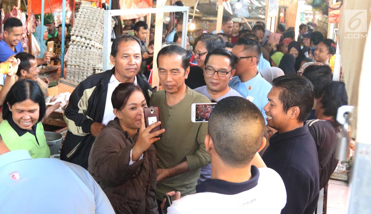 Calon Presiden nomor urut 01 Joko Widodo atau Jokowi berswafoto dengan pengunjung saat melakukan blusukan ke Pasar Cihaurgeulis, Bandung, Minggu (11/11). Jokowi terlihat ditemani oleh Gubernur Jawa Barat Ridwan Kamil. (Liputan6.com/Angga Yuniar)