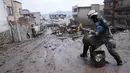 Petugas menggunakan ember untuk membuang lumpur sehari setelah lereng bukit yang diguyur hujan runtuh dan membawa gelombang lumpur ke rumah-rumah dan lapangan olahraga, di lingkungan La Gasca di Quito, Ekuador, Rabu (2/2/2022). Tanah longsor menewaskan sedikitnya 24 orang. (AP Photo/Dolores Ochoa)