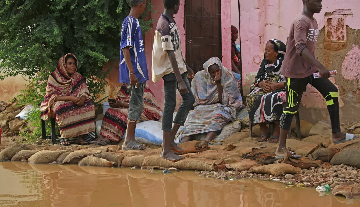 Penduduk Sudan duduk di luar rumah mereka yang banjir di daerah alqamayir di kota kembar ibu kota Omdurman (26/8/2020). (AFP Photo/Ashraf Shazly)