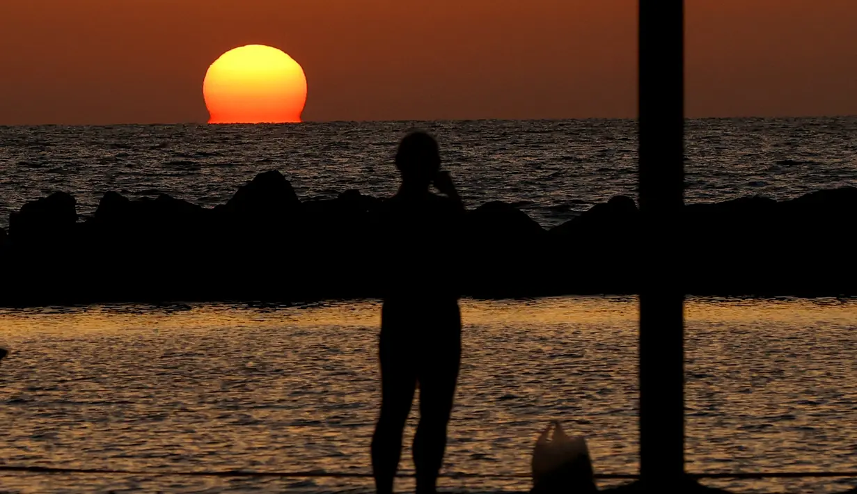 Seorang warga menyaksikan matahari terbenam di kota pesisir Mediterania Israel Netanya, utara Tel Aviv (8/6/2021). Kota ini memiliki penduduk sebanyak 173.300. (AFP/ Jack Guez)