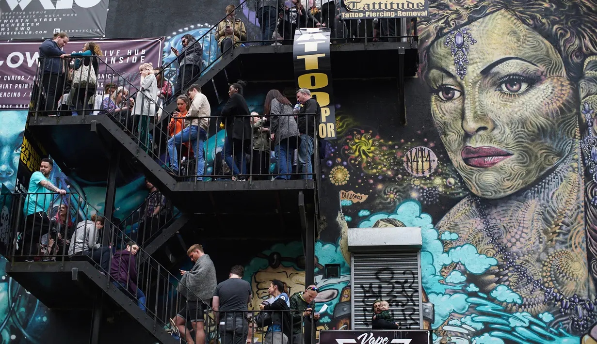 Sejumlah orang mengantre untuk membuat tato bergambar lebah di Manchester (28/5). Seniman ini membuat tato lebah untuk menggalang dana yang diberikan kepada korban serangan bom konser Ariana Grande. (AP Photo/Mstyslav Chernov)