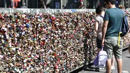 Warga melewati gembok cinta di sebuah jembatan di Cologne, Jerman, Rabu, (5/8/2020). Sebagai bukti cinta mereka, puluhan ribu pasangan telah memasang gembok selama bertahun-tahun ke pagar di Jembatan Hohenzollern sebelum melemparkan kunci ke dalam Sungai Rhein di bawah. (AP Photo/ Martin Meissner)