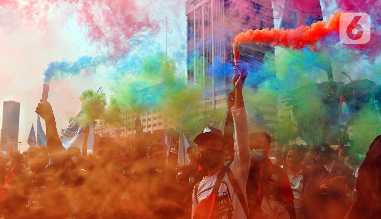 Sejumlah buruh menyalakan suar saat melakukan unjuk rasa di depan Gedung DPR, Jakarta, Rabu (10/8/2022). Dalam aksi tersebut mereka menuntut agar pemerintah menghapus Omnibus Law. (Liputan6.com/Angga Yuniar)