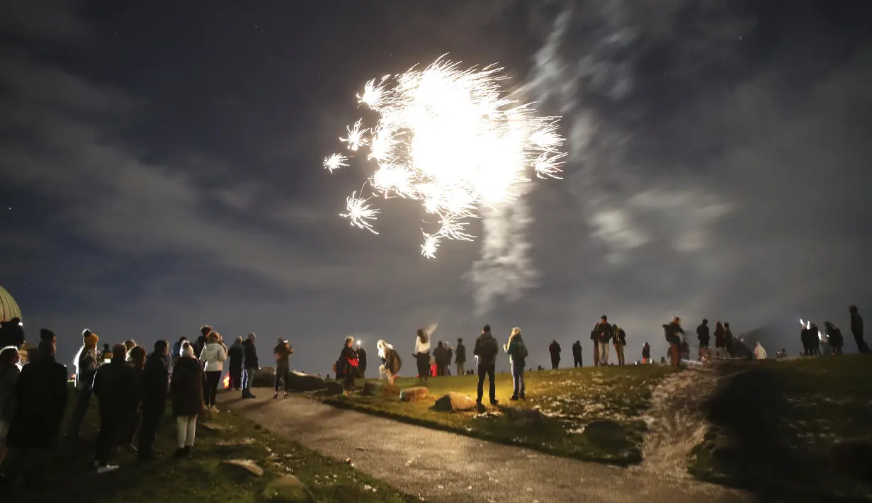 Orang-orang di Calton Hill menonton kembang api di Edinburgh ketika orang-orang didesak untuk menghindari perayaan Hogmanay di tengah pembatasan ketat virus corona pada Kamis, 31 Desember 2020. (Andrew Milligan / PA via AP)