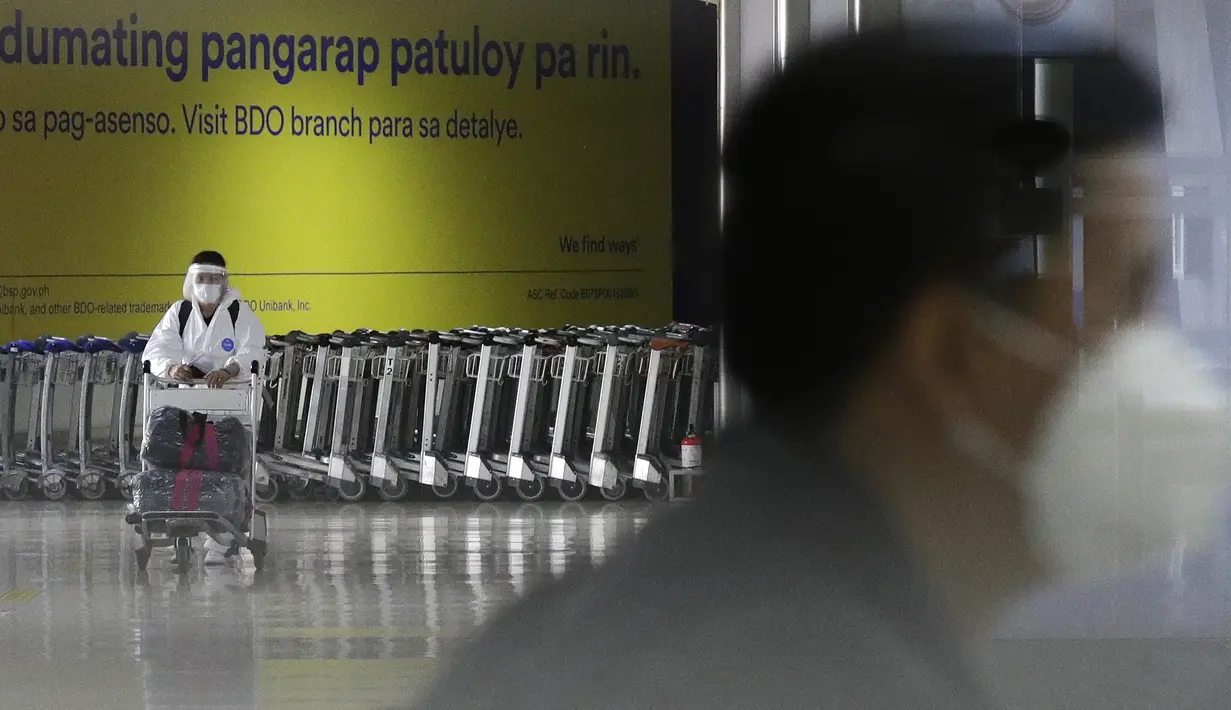 Seorang perempuan dengan pakaian pelindung mendorong troli di area kedatangan Bandara Internasional Manila, Rabu (17/3/2021). Filipina memutuskan melarang masuknya warga negara asing sementara waktu dan membatasi warga Filipina yang kembali untuk menahan lonjakan COVID-19. (AP Photo/Aaron Favila)