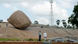 Pengunjung berdiri dekat batu 'Krishna's Butter Ball' di Mahabalipuram, India, Kamis (3/10/2019). Menurut mitos masyarakat Hindu posisi batu itu dikaitkan legenda Dewa Krishna yang berusaha mencuri mentega dari dalam toples milik ibunya. (ARUN SANKAR / AFP)