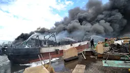 Petugas pemadam kebakaran dibantu pekerja mencoba memadamkan api di kapal nelayan di Pelabuhan Benoa, Denpasar, Bali, Senin (9/7). Upaya pemadaman melibatkan 11 unit mobil pemadam kebakaran. (SONNY TUMBELAKA/AFP)