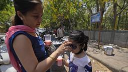 Seorang perempuan mengenakan kacamata hitam untuk anaknya pada hari yang panas di New Delhi, India, Sabtu, 14 Mei 2022. Suhu di New Delhi mencapai 45 Derajat Celcius. (AP Photo/Manish Swarup)