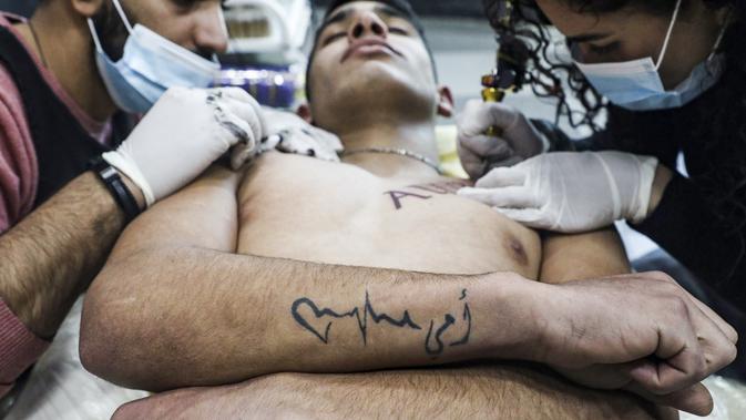 Naim Abdallah dibantu oleh seorang asisten saat menuangkan kreasinya di atas tubuh klien di ruang kerjanya di Kota Betlehem di Tepi Barat (24/1/2021). (AFP/Hazem Bader)