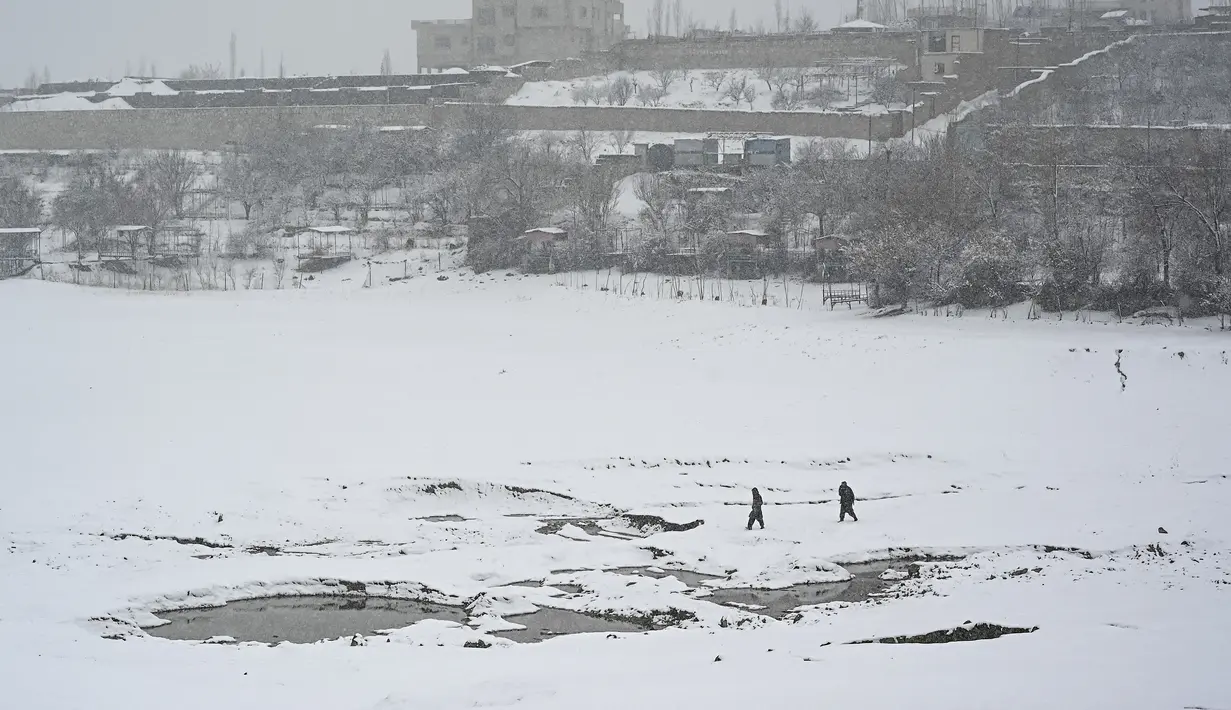 Orang-orang berjalan di dekat danau Qargha saat hujan salju di Kabul (4/1/2022). Sedikitnya tujuh warga Afghanistan tewas dan 26 lainnya cedera dalam beberapa kecelakaan lalu lintas. (AFP/Mohd Rasfan)
