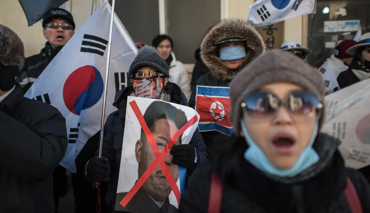 Pengunjuk rasa anti-Korea Utara membawa poster Kim Jong-Un saat menggelar aksi di pelabuhan Mukho di Donghae, Korea Selatan (6/2). Sekitar 120 seniman dari Korut akan tampil di Olimpiade Musim Dingin Pyeongchang 2018. (AFP/Ed Jones)