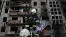 Petugas pemadam kebakaran Ukraina memegang sebuah foto, ditemukan di puing-puing, saat mereka bekerja di sebuah bangunan penduduk setelah terkena tembakan artileri Rusia di Kiev, Senin, 14 Maret 2022. (AP Photo/Vadim Ghirda)
