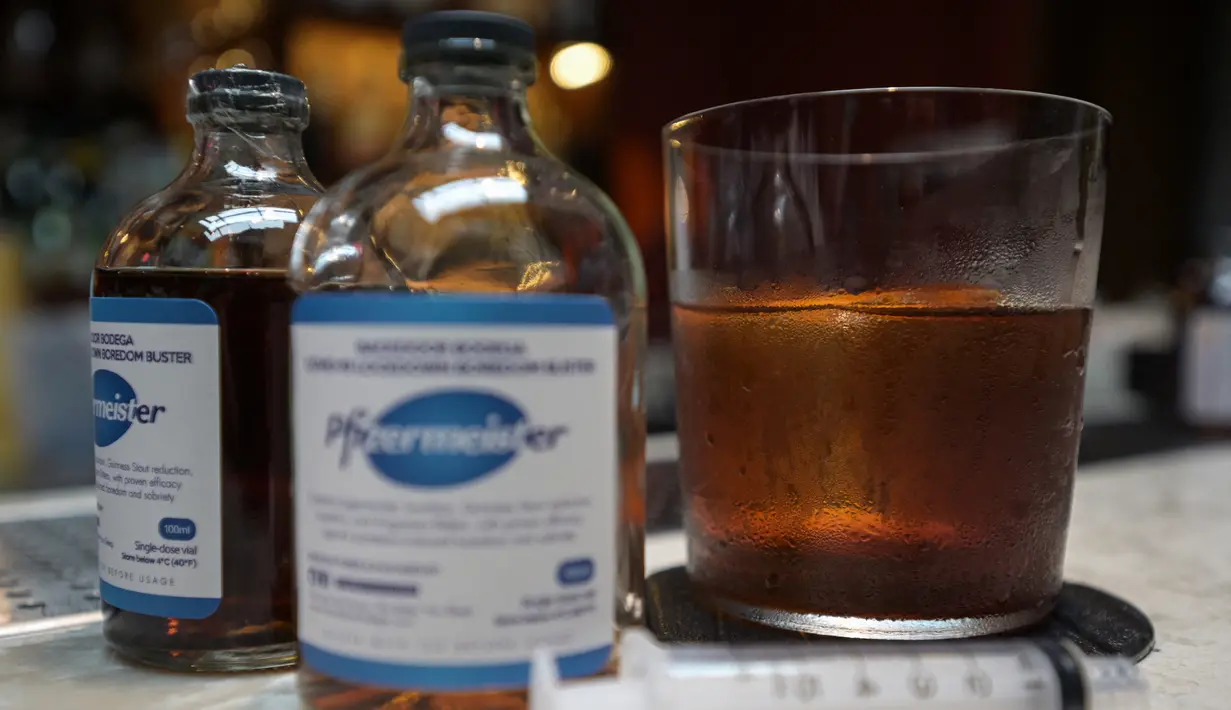Segelas minuman Pfizermeister, minuman yang terinspirasi oleh vaksin virus corona Covid-19, di samping botolnya di sebuah bar koktail di George Town di pulau Penang, Malaysia (8/9/2021). (AFP/Mohd Rasfan)