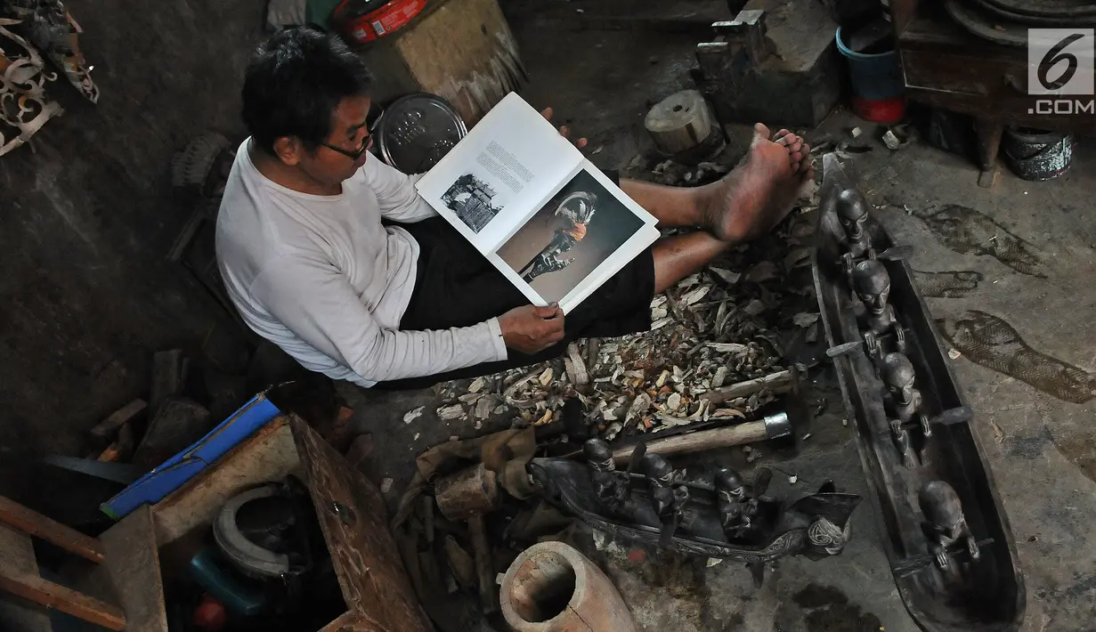Perajin Oman Sumarna melihat buku untuk panduan membuat patung di Sanggar Primitif, Sawangan, Depok, Rabu (9/1). Sanggar kerajinan pahatan kayu tradisional itu mengambil tema-tema primitif untuk melestarikan budaya Indonesia (Liputan6.com/Herman Zakharia)