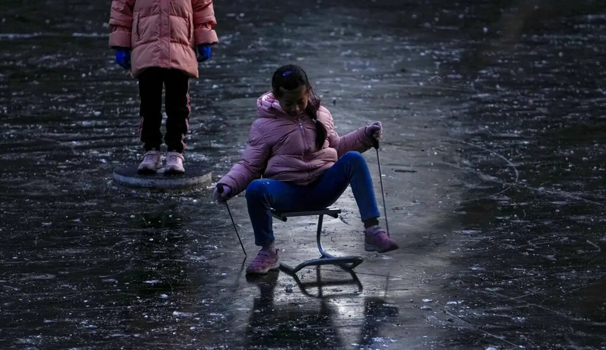 Seorang anak bermanuver di atas kereta luncur yang dibuat khusus saat bermain di sungai yang membeku dekat area perumahan, Beijing, China, 3 Januari 2022. Libur Tahun Baru dimanfaatkan warga untuk bermain ice skating di sungai dan danau yang membeku. (AP Photo/Andy Wong)