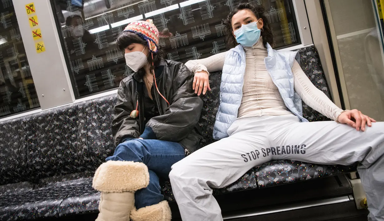 Elena Buscaino (kanan) dan Mina Bonakdar berpose dengan Riot Pants bertuliskan "Stop Spreading" di kereta bawah tanah di Berlin, 5 Februari 2021. Aktivis feminis itu dalam misi menghentikan kebiasaan penumpang pria melebarkan kaki saat duduk sehingga memakan dua kursi kereta. (STEFANIE LOOS/AFP)