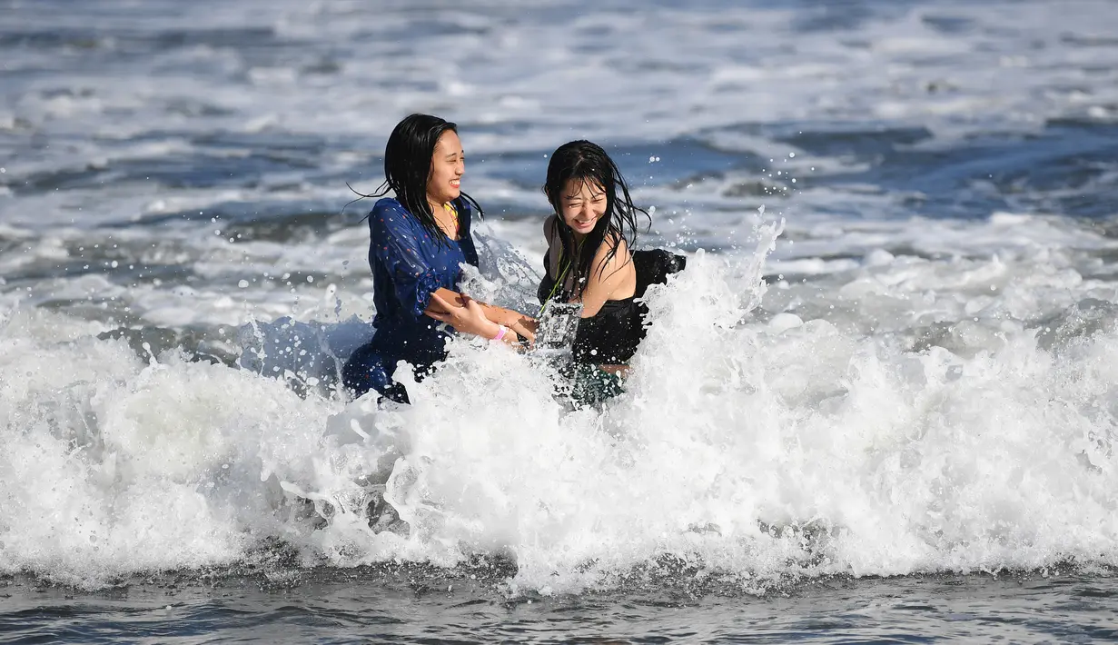 Dua wanita menikmati ombak di sepanjang pantai dekat Pulau Enoshima di pantai Prefektur Kanagawa, barat daya Tokyo (13/8/2019). Enoshima adalah pulau lepas pantai kecil, sekitar 4 km di sekelilingnya, di mulut Sungai Katase yang mengalir ke Teluk Sagami di Prefektur Kanagawa, Jepang. (AFP Photo/Char
