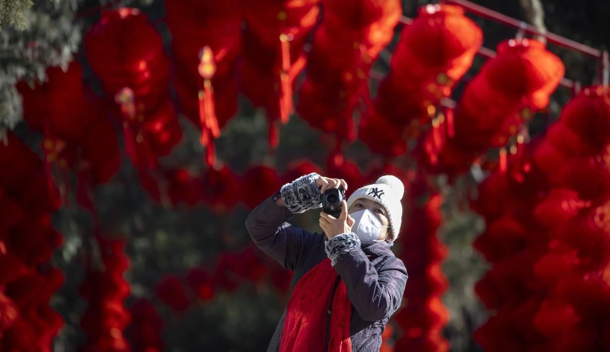 Seorang wanita mengenakan masker mengambil foto di dekat jalan setapak yang dihiasi lentera untuk Tahun Baru Imlek mendatang di sebuah taman umum di Beijing, Jumat, 20 Januari 2023. Tahun Kelinci secara resmi dimulai pada 22 Januari. (AP Photo/Mark Schiefelbein)