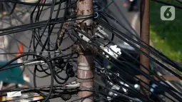 Kabel listrik dan kabel optik yang terlihat semrawut di kawasan Taman Puring, Jakarta, Jumat (3/7/2020). Kesemrawutan kabel ini sering terlihat di sejumlah kawasan Jakarta yang menyebabkan keindahan menjadi hilang dan pemandangan kurang enak untuk dilihat. (Liputan6.com/Johan Tallo)