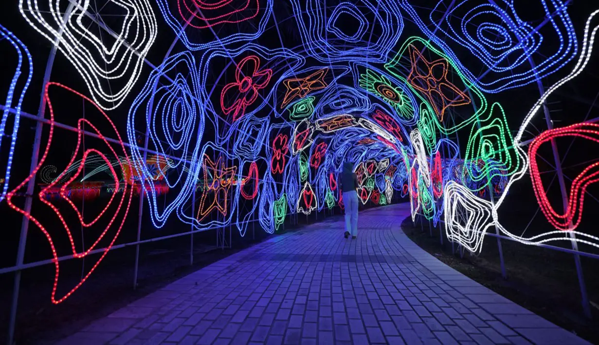 Seorang wanita berjalan melewati instalasi lampu di Dubai Garden Glow, Dubai, Uni Emirat Arab, 1 November 2021. Instalasi tersebut dibuat dari lebih satu juta bohlam penghemat energi dan kain bercahaya daur ulang karya seniman seluruh dunia. (GIUSEPPE CACACE/AFP)