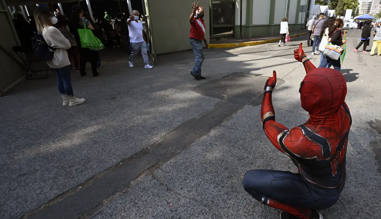Seorang pria yang mengenakan kostum Spiderman menyapa orang-orang setelah mereka disuntik vaksin covid-19 Pfizer-BioNTech di Mexico City, Meksiko, Selasa (28/12/2021). Spiderman tersebut dipekerjakan oleh Pemerintah Kota untuk menghibur para peserta vaksinasi. (ALFREDO ESTRELLA / AFP)