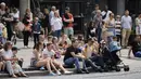 Orang-orang duduk di trotoar menonton artis jalanan di Covent Garden, pusat kota London, Kamis (3/6/2021). Pemerintah Inggris belum bisa memastikan akan sepenuhnya mencabut lockdown yang berakhir pada 21 Juni nanti meski kasus Covid-19 mengalami tren penurunan. (Tolga Akmen/AFP)