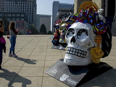 Warga berswafoto pada pameran Fridacraneos, tengkorak raksasa yang dilukis untuk menghormati mendiang seniman Meksiko Frida Kahlo, sebagai bagian dari perayaan Hari Kematian di Monumen Revolusi, Mexico City, Meksiko, 29 Oktober 2021. (Claudio CRUZ/AFP)