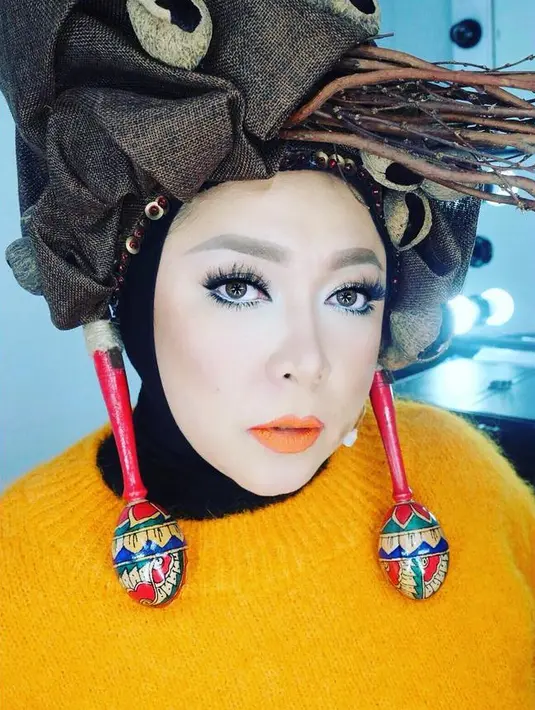 Tampilan Melly begitu nyentrik dengan sweater berwarna oranye dan headpiece yang unik dari Ms Fresh Lemonade by Moly. Hijab hitamnya dibalut headpiece berhiaskan ranting-ranting dan deretan buah keluek. (Instagram/melly_goeslaw)