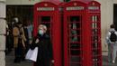 Seorang wanita melewati kotak telepon merah ikonik di distrik Covent Garden, pusat kota London, Senin (29/11/2021). Di Inggris, kewajiban mengenakan masker akan berlaku lagi di toko-toko dan transportasi umum mulai Selasa menyusul temuan Covid-19 varian Omicron. (AP Photo/Matt Dunham)