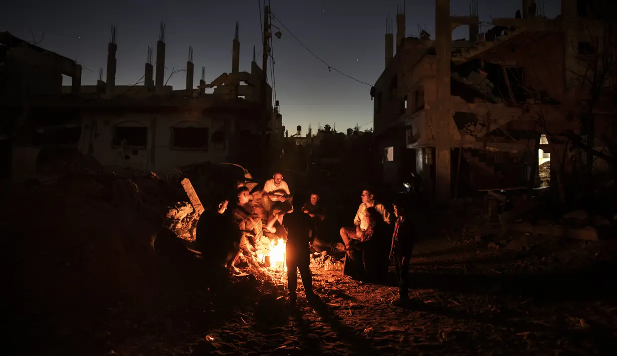 Warga Palestina duduk di sekitar api saat mereka bermalam di samping rumah mereka yang hancur di kota Beit Hanoun, Jalur Gaza utara, Rabu (26/5/2021). Serangan udara Israel selama 11 hari ke Jalur Gaza mengakibatkan ratusan jiwa tewas, ribuan rumah dan bangunan hancur. (AP Photo/Khalil Hamra)