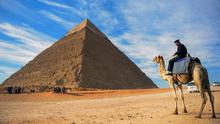 Seorang pria menunggang unta dengan latar belakang piramida Khafre yang berada di dataran tinggi Giza di pinggiran barat daya ibukota Kairo, Mesir (6/12). (AFP Photo/Mohamed El-Shahed)