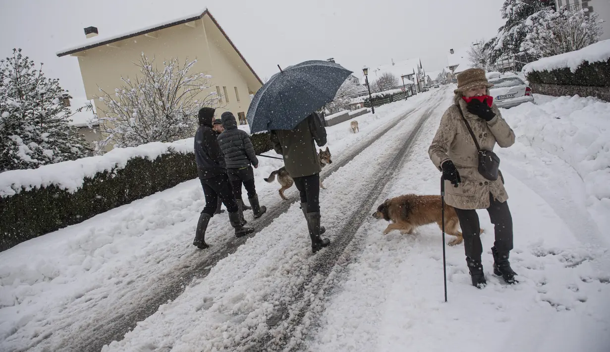 Orang-orang berjalan dengan anjing mereka di salju di Burguete, Spanyol utara, Senin, 16 Januari 2023. Pihak berwenang telah mengumumkan salju dan suhu sangat rendah selama beberapa hari ke depan di seluruh bagian utara negara itu. (AP Photo/Alvaro Barrientos)