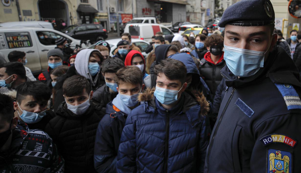 Polisi berdiri di depan remaja yag antre di luar restoran untuk mendapatkan burger gratis yang ditawarkan selama promosi di Bucharest, Rumania, Senin (1/2/2021). Ratusan orang berkerumun demi burger gratis hingga polisi mendenda restoran karena tidak mematuhi protokol COVID-19. (AP/Vadim Ghirda)