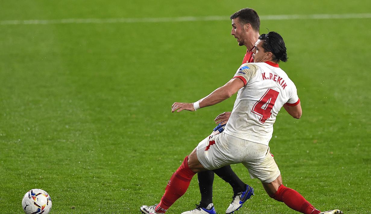 Gelandang Osasuna, Oier Sanjurjo (kiri) melepaskan umpan dibayangi bek Sevilla, Karim Rekik dalam laga lanjutan Liga Spanyol 2020/21 pekan ke-24 di El Sadar Stadium, Plampona, Senin (22/2/2021). Osasuna akaah 0-2 dari Sevilla. (AFP/Ander Gillenea)